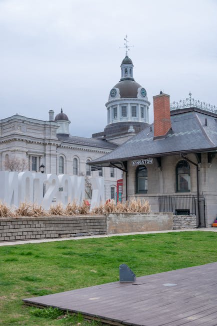 Exterior view of Kingston railway station with historic architecture, including a prominent domed clock tower and ornate details, under an overcast sky. The station building features a dark slate roof